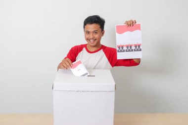 Heyecanlı Asyalı adamın portresi oy pusulasını sandığa yerleştirip koyuyor. Endonezya cumhurbaşkanı ve hükümeti için genel seçimler veya Pemilu. Beyaz arkaplanda izole edilmiş resim