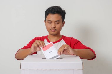 Heyecanlı Asyalı adamın portresi oy pusulasını sandığa yerleştirip koyuyor. Endonezya cumhurbaşkanı ve hükümeti için genel seçimler veya Pemilu. Beyaz arkaplanda izole edilmiş resim