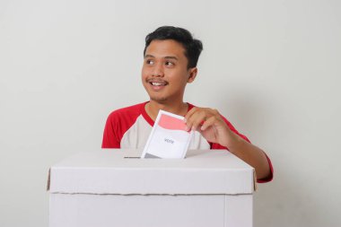 Heyecanlı Asyalı adamın portresi oy pusulasını sandığa yerleştirip koyuyor. Endonezya cumhurbaşkanı ve hükümeti için genel seçimler veya Pemilu. Beyaz arkaplanda izole edilmiş resim