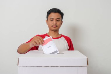 Heyecanlı Asyalı adamın portresi oy pusulasını sandığa yerleştirip koyuyor. Endonezya cumhurbaşkanı ve hükümeti için genel seçimler veya Pemilu. Beyaz arkaplanda izole edilmiş resim