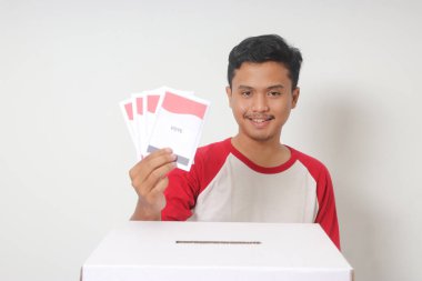 Heyecanlı Asyalı adamın portresi oy pusulasını sandığa yerleştirip koyuyor. Endonezya cumhurbaşkanı ve hükümeti için genel seçimler veya Pemilu. Beyaz arkaplanda izole edilmiş resim