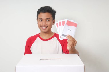 Heyecanlı Asyalı adamın portresi oy pusulasını sandığa yerleştirip koyuyor. Endonezya cumhurbaşkanı ve hükümeti için genel seçimler veya Pemilu. Beyaz arkaplanda izole edilmiş resim