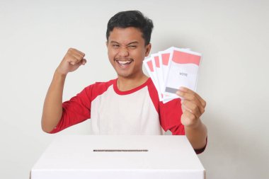 Heyecanlı Asyalı adamın portresi oy pusulasını sandığa yerleştirip koyuyor. Endonezya cumhurbaşkanı ve hükümeti için genel seçimler veya Pemilu. Beyaz arkaplanda izole edilmiş resim