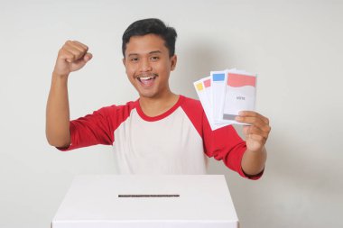 Heyecanlı Asyalı adamın portresi oy pusulasını sandığa yerleştirip koyuyor. Endonezya cumhurbaşkanı ve hükümeti için genel seçimler veya Pemilu. Beyaz arkaplanda izole edilmiş resim