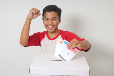 Heyecanlı Asyalı adamın portresi oy pusulasını sandığa yerleştirip koyuyor. Endonezya cumhurbaşkanı ve hükümeti için genel seçimler veya Pemilu. Beyaz arkaplanda izole edilmiş resim