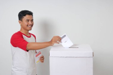 Heyecanlı Asyalı adamın portresi oy pusulasını sandığa yerleştirip koyuyor. Endonezya cumhurbaşkanı ve hükümeti için genel seçimler veya Pemilu. Beyaz arkaplanda izole edilmiş resim