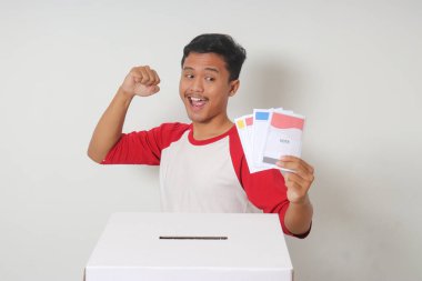 Heyecanlı Asyalı adamın portresi oy pusulasını sandığa yerleştirip koyuyor. Endonezya cumhurbaşkanı ve hükümeti için genel seçimler veya Pemilu. Beyaz arkaplanda izole edilmiş resim