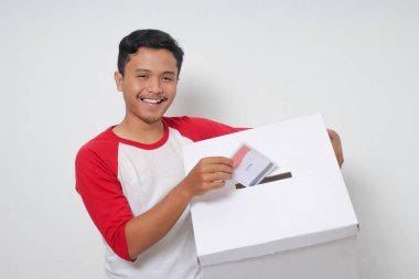 Heyecanlı Asyalı adamın portresi oy pusulasını sandığa yerleştirip koyuyor. Endonezya cumhurbaşkanı ve hükümeti için genel seçimler veya Pemilu. Beyaz arkaplanda izole edilmiş resim