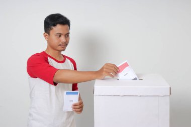 Heyecanlı Asyalı adamın portresi oy pusulasını sandığa yerleştirip koyuyor. Endonezya cumhurbaşkanı ve hükümeti için genel seçimler veya Pemilu. Beyaz arkaplanda izole edilmiş resim