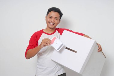 Heyecanlı Asyalı adamın portresi oy pusulasını sandığa yerleştirip koyuyor. Endonezya cumhurbaşkanı ve hükümeti için genel seçimler veya Pemilu. Beyaz arkaplanda izole edilmiş resim