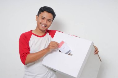 Heyecanlı Asyalı adamın portresi oy pusulasını sandığa yerleştirip koyuyor. Endonezya cumhurbaşkanı ve hükümeti için genel seçimler veya Pemilu. Beyaz arkaplanda izole edilmiş resim