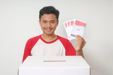 Heyecanlı Asyalı adamın portresi oy pusulasını sandığa yerleştirip koyuyor. Endonezya cumhurbaşkanı ve hükümeti için genel seçimler veya Pemilu. Beyaz arkaplanda izole edilmiş resim