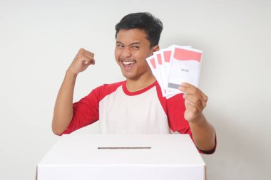 Heyecanlı Asyalı adamın portresi oy pusulasını sandığa yerleştirip koyuyor. Endonezya cumhurbaşkanı ve hükümeti için genel seçimler veya Pemilu. Beyaz arkaplanda izole edilmiş resim