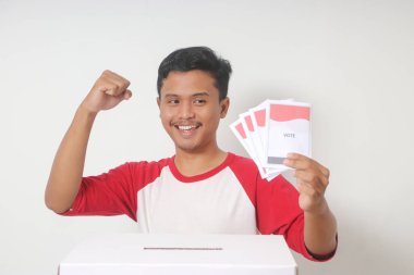 Heyecanlı Asyalı adamın portresi oy pusulasını sandığa yerleştirip koyuyor. Endonezya cumhurbaşkanı ve hükümeti için genel seçimler veya Pemilu. Beyaz arkaplanda izole edilmiş resim