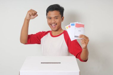 Heyecanlı Asyalı adamın portresi oy pusulasını sandığa yerleştirip koyuyor. Endonezya cumhurbaşkanı ve hükümeti için genel seçimler veya Pemilu. Beyaz arkaplanda izole edilmiş resim