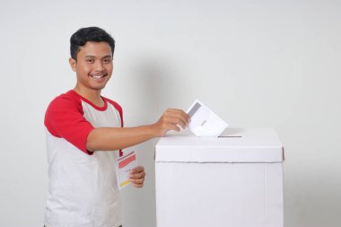 Heyecanlı Asyalı adamın portresi oy pusulasını sandığa yerleştirip koyuyor. Endonezya cumhurbaşkanı ve hükümeti için genel seçimler veya Pemilu. Beyaz arkaplanda izole edilmiş resim