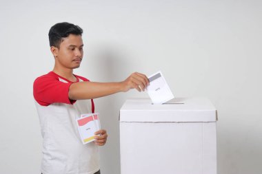 Heyecanlı Asyalı adamın portresi oy pusulasını sandığa yerleştirip koyuyor. Endonezya cumhurbaşkanı ve hükümeti için genel seçimler veya Pemilu. Beyaz arkaplanda izole edilmiş resim