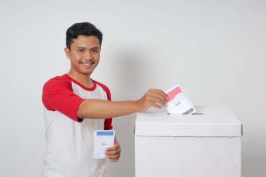 Heyecanlı Asyalı adamın portresi oy pusulasını sandığa yerleştirip koyuyor. Endonezya cumhurbaşkanı ve hükümeti için genel seçimler veya Pemilu. Beyaz arkaplanda izole edilmiş resim