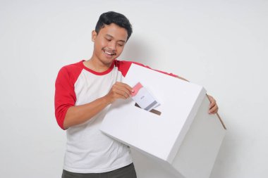 Heyecanlı Asyalı adamın portresi oy pusulasını sandığa yerleştirip koyuyor. Endonezya cumhurbaşkanı ve hükümeti için genel seçimler veya Pemilu. Beyaz arkaplanda izole edilmiş resim