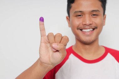 Heyecanlı Asyalı adamın portresi genel seçimlerden sonra mor mürekkebe batırılmış küçük parmağını gösteriyor ya da Endonezya devlet başkanı ve hükümeti için Pemilu 'yu. Beyaz arkaplanda izole