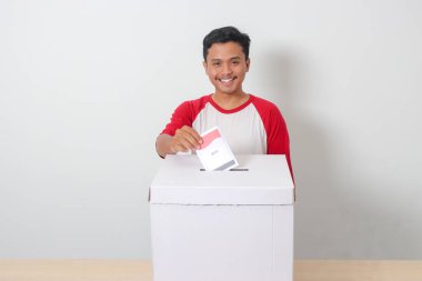 Heyecanlı Asyalı adamın portresi oy pusulasını sandığa yerleştirip koyuyor. Endonezya cumhurbaşkanı ve hükümeti için genel seçimler veya Pemilu. Beyaz arkaplanda izole edilmiş resim