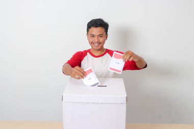 Heyecanlı Asyalı adamın portresi oy pusulasını sandığa yerleştirip koyuyor. Endonezya cumhurbaşkanı ve hükümeti için genel seçimler veya Pemilu. Beyaz arkaplanda izole edilmiş resim