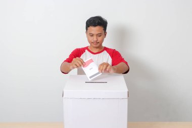 Heyecanlı Asyalı adamın portresi oy pusulasını sandığa yerleştirip koyuyor. Endonezya cumhurbaşkanı ve hükümeti için genel seçimler veya Pemilu. Beyaz arkaplanda izole edilmiş resim