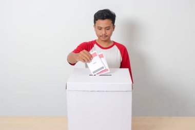 Heyecanlı Asyalı adamın portresi oy pusulasını sandığa yerleştirip koyuyor. Endonezya cumhurbaşkanı ve hükümeti için genel seçimler veya Pemilu. Beyaz arkaplanda izole edilmiş resim