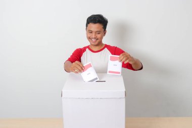 Heyecanlı Asyalı adamın portresi oy pusulasını sandığa yerleştirip koyuyor. Endonezya cumhurbaşkanı ve hükümeti için genel seçimler veya Pemilu. Beyaz arkaplanda izole edilmiş resim