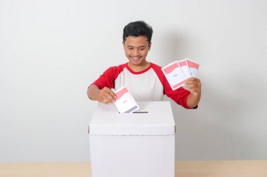 Heyecanlı Asyalı adamın portresi oy pusulasını sandığa yerleştirip koyuyor. Endonezya cumhurbaşkanı ve hükümeti için genel seçimler veya Pemilu. Beyaz arkaplanda izole edilmiş resim