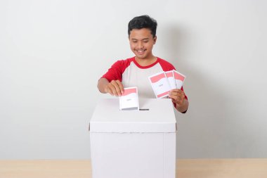 Heyecanlı Asyalı adamın portresi oy pusulasını sandığa yerleştirip koyuyor. Endonezya cumhurbaşkanı ve hükümeti için genel seçimler veya Pemilu. Beyaz arkaplanda izole edilmiş resim