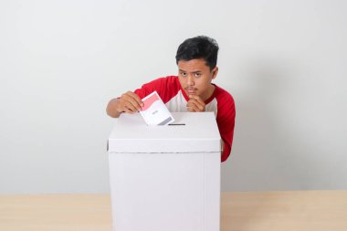 Heyecanlı Asyalı adamın portresi oy pusulasını sandığa yerleştirip koyuyor. Endonezya cumhurbaşkanı ve hükümeti için genel seçimler veya Pemilu. Beyaz arkaplanda izole edilmiş resim