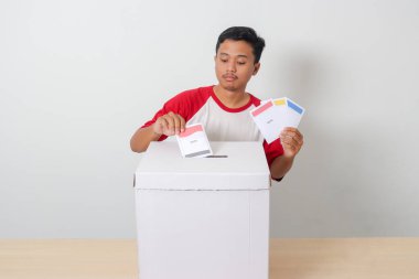Heyecanlı Asyalı adamın portresi oy pusulasını sandığa yerleştirip koyuyor. Endonezya cumhurbaşkanı ve hükümeti için genel seçimler veya Pemilu. Beyaz arkaplanda izole edilmiş resim