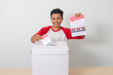 Heyecanlı Asyalı adamın portresi oy pusulasını sandığa yerleştirip koyuyor. Endonezya cumhurbaşkanı ve hükümeti için genel seçimler veya Pemilu. Beyaz arkaplanda izole edilmiş resim