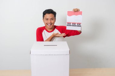 Heyecanlı Asyalı adamın portresi oy pusulasını sandığa yerleştirip koyuyor. Endonezya cumhurbaşkanı ve hükümeti için genel seçimler veya Pemilu. Beyaz arkaplanda izole edilmiş resim
