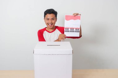 Heyecanlı Asyalı adamın portresi oy pusulasını sandığa yerleştirip koyuyor. Endonezya cumhurbaşkanı ve hükümeti için genel seçimler veya Pemilu. Beyaz arkaplanda izole edilmiş resim