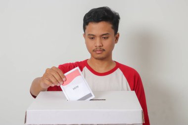 Heyecanlı Asyalı adamın portresi oy pusulasını sandığa yerleştirip koyuyor. Endonezya cumhurbaşkanı ve hükümeti için genel seçimler veya Pemilu. Beyaz arkaplanda izole edilmiş resim