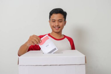Heyecanlı Asyalı adamın portresi oy pusulasını sandığa yerleştirip koyuyor. Endonezya cumhurbaşkanı ve hükümeti için genel seçimler veya Pemilu. Beyaz arkaplanda izole edilmiş resim