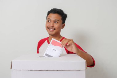 Heyecanlı Asyalı adamın portresi oy pusulasını sandığa yerleştirip koyuyor. Endonezya cumhurbaşkanı ve hükümeti için genel seçimler veya Pemilu. Beyaz arkaplanda izole edilmiş resim