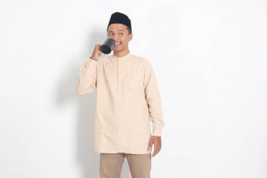 Koko tişörtlü çekici Asyalı Müslüman adamın portresi. Kaslı, fincanı tutan, içme suyu içen, oruç tuttuktan sonra susuzluğunu gideren. Beyaz arkaplanda izole edilmiş resim