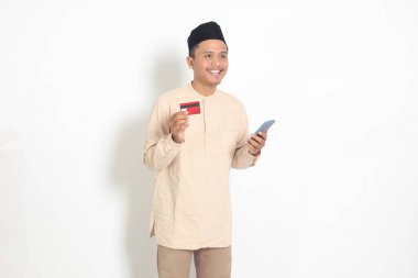 Elinde cep telefonu olan ve kredi kartı sunan Koko tişörtlü yakışıklı Asyalı Müslüman adamın portresi. Beyaz arkaplanda izole edilmiş resim