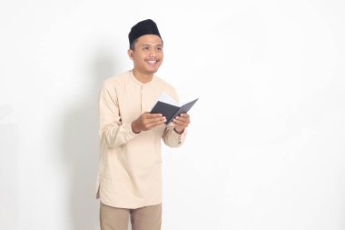 Koko tişörtlü heyecanlı müslüman adamın portresi. Defterinde peci yazıyor. Mutlu Asyalı adam not alıyor. Beyaz arkaplanda izole edilmiş resim