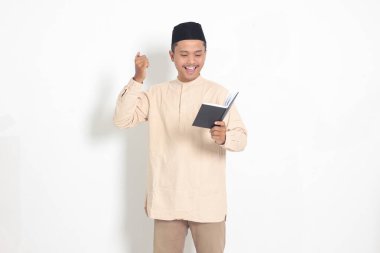 Koko tişörtlü heyecanlı müslüman adamın portresi. Defterinde peci yazıyor. Mutlu Asyalı adam not alıyor. Beyaz arkaplanda izole edilmiş resim