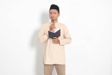 Kafası karışmış Koko gömlekli Asyalı Müslüman adamın portresi. Peci kitabı okuyor, çenesine kalem tutarak başka yere bakan bir fikir düşünüyor. Beyaz arkaplanda izole edilmiş resim