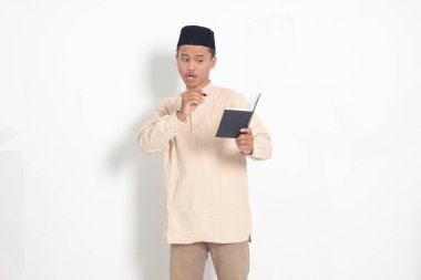 Koko tişörtlü heyecanlı müslüman adamın portresi. Defterinde peci yazıyor. Mutlu Asyalı adam not alıyor. Beyaz arkaplanda izole edilmiş resim