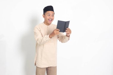 Koko tişörtlü heyecanlı müslüman adamın portresi. Defterinde peci yazıyor. Mutlu Asyalı adam not alıyor. Beyaz arkaplanda izole edilmiş resim