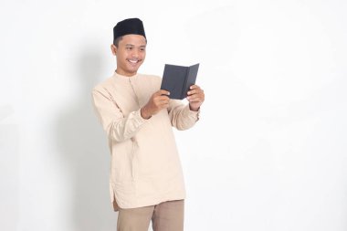 Koko gömlekli çekici Asyalı Müslüman adamın portresi. Peci kitabı okuyor. Beyaz arkaplanda izole edilmiş resim