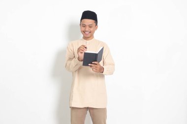 Koko tişörtlü heyecanlı müslüman adamın portresi. Defterinde peci yazıyor. Mutlu Asyalı adam not alıyor. Beyaz arkaplanda izole edilmiş resim