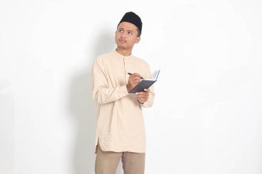 Kafası karışmış Koko gömlekli Asyalı Müslüman adamın portresi. Peci kitabı okuyor, çenesine kalem tutarak başka yere bakan bir fikir düşünüyor. Beyaz arkaplanda izole edilmiş resim