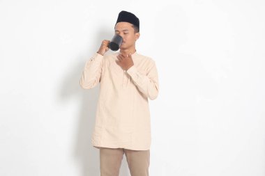 Koko tişörtlü çekici Asyalı Müslüman adamın portresi. Kaslı, fincanı tutan, içme suyu içen, oruç tuttuktan sonra susuzluğunu gideren. Beyaz arkaplanda izole edilmiş resim